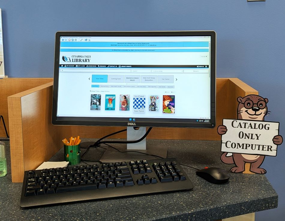 A computer with the library's book catalog on it. A printed otter holding a sign that says Catalog Only Computer.
