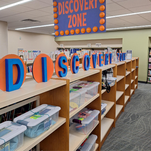 Library shelves filled with small toes with signs saying Discover Zone above them